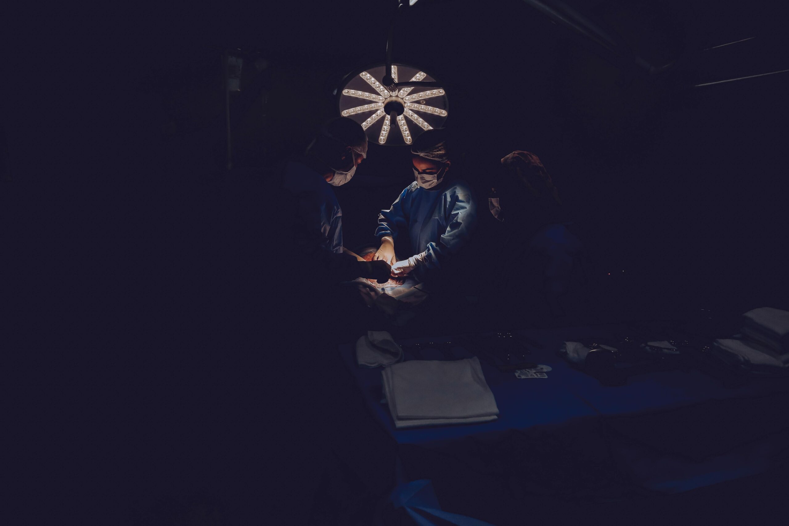 A team of surgeons focuses intently on a procedure in a dimly lit operating room, emphasizing precision and skill.
